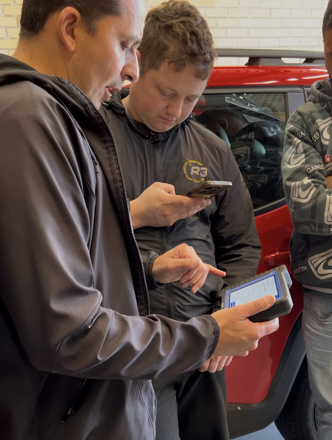 Mecânicos da R3 conferindo um diagnóstico com scanner e celular ao lado de um Renegade vermelho